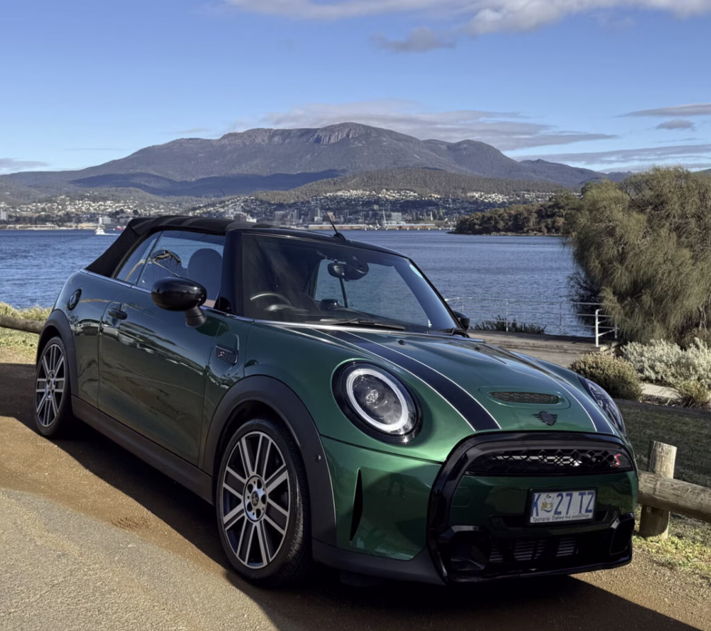 A green Mini is parked in front of kunanyi / Mt Wellington in Hobart, Australia. It's a sunny day and we can see the water in the background.